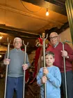 Tres generaciones de vecinos posan con varas procesionales junto a una imagen, reflejo del relevo y la continuidad de la tradici&oacute;n cofrade en la Casa de Novenas.