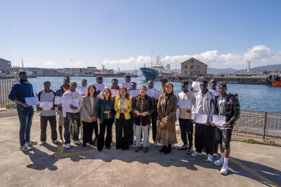 Participantes del curso de formaci&oacute;n prelaboral impulsado por Stella Maris posan junto a la conselleira do Mar, Marta Villaverde, tras la entrega de diplomas celebrada en un entorno portuario gallego.