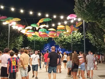 Ambiente festivo en Mondariz durante as festas de San Roque e da Virxe da Pe&ntilde;a de Francia, con veci&ntilde;os e visitantes gozando da m&uacute;sica e da iluminaci&oacute;n ornamental na vila.
