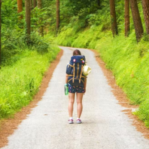 Una viajera avanza con su mochila por un sendero desconocido, símbolo de quienes buscan un nuevo destino sin dejar de cargar con su historia.