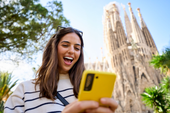 Una joven consulta su tel&eacute;fono m&oacute;vil frente a la Sagrada Familia de Barcelona, una de las ciudades espa&ntilde;olas que concentra un creciente n&uacute;mero de n&oacute;madas digitales en 2026.