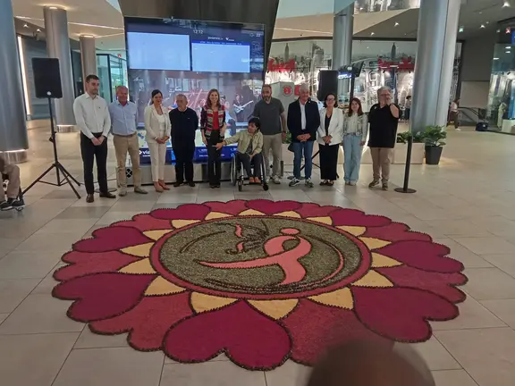 Representantes institucionales, entidades sociales y miembros de la Asociaci&oacute;n de Alfombristas do Corpus Christi de Ponteareas posan junto a la alfombra floral solidaria instalada en Vialia Vigo, dedicada a la lucha contra el c&aacute;ncer de mama.