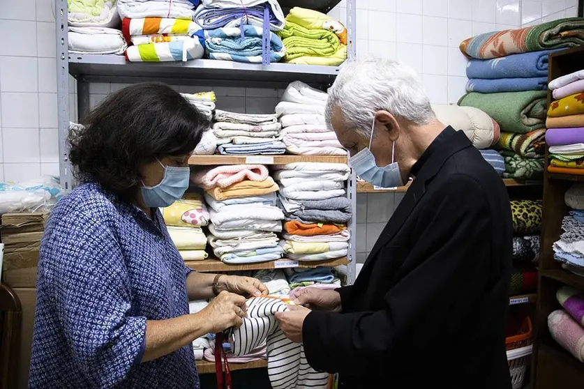 Elena, una de las trabajadoras social, junto con Adoración, fundadora de AYUVI, presentan el almacén readaptado al obispo Quinteiro Fiuza.