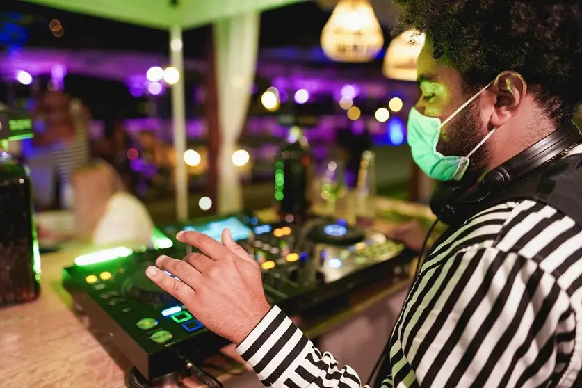 Young african DJ man mixing music at club outdoor while wearing safety face mask for coronavirus outbreak