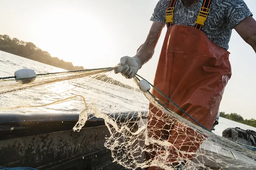 Dynamic composition with a fisherman dressed in an orange rompers gathering his trammel net during a fishing trip on the Danube river.