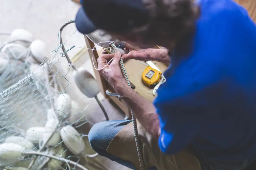 An Alaskan fisherman prepares and checks gill nets in his work space The shot is over his left shoulder.