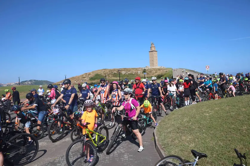 El pelotón de ciclistas colorea el paseo marítimo, con la majestuosa Torre de Hércules como telón de fondo. ¡A Coruña en estado puro!