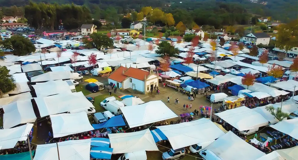 Vista cenital de la Feria de los Santos de Cerdal, con los coloridos puestos rodeando la capilla de San Antonio, epicentro de esta cita tradicional en Valença.
