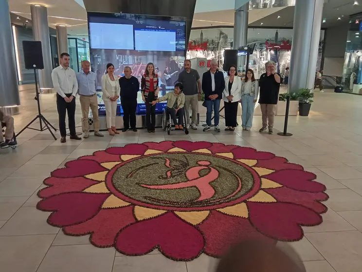 Representantes institucionales, entidades sociales y miembros de la Asociaci&oacute;n de Alfombristas do Corpus Christi de Ponteareas posan junto a la alfombra floral solidaria instalada en Vialia Vigo, dedicada a la lucha contra el c&aacute;ncer de mama.