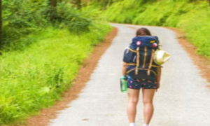 Una viajera avanza con su mochila por un sendero desconocido, símbolo de quienes buscan un nuevo destino sin dejar de cargar con su historia.