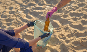 Una persona recoge una botella de pl&aacute;stico de la arena, un gesto sencillo que contribuye a reducir los residuos y proteger los ecosistemas costeros.