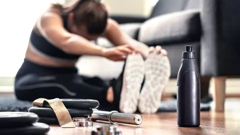 Mujer estirando los músculos antes de entrenamiento de gimnasio y entrenamiento con pesas en la sala de estar en casa. Atleta de fitness femenino haciendo calentamiento y ejercicio físico. Calentamiento antes de hacer ejercicio. Ropa deportiva y zapatillas de deporte.