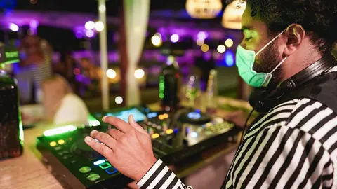 Young african DJ man mixing music at club outdoor while wearing safety face mask for coronavirus outbreak