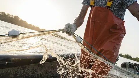 Dynamic composition with a fisherman dressed in an orange rompers gathering his trammel net during a fishing trip on the Danube river.