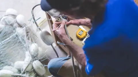 An Alaskan fisherman prepares and checks gill nets in his work space The shot is over his left shoulder.