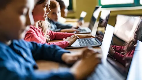 Happy schoolgirl and her classmates e-learning over laptops during a class in the classroom.
