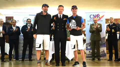 El patrón y tripulante del 'Orión' reciben el premio de vencedor en clase 1 de manos del Comandante Director de la Escuela Naval, CN Pedro Cardona Suanzes.