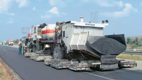 Un camión de asfaltado trabaja en la rehabilitación de una carretera, parte del plan del Ministerio de Transportes para renovar 114 km de la Red de Carreteras del Estado con materiales sostenibles.