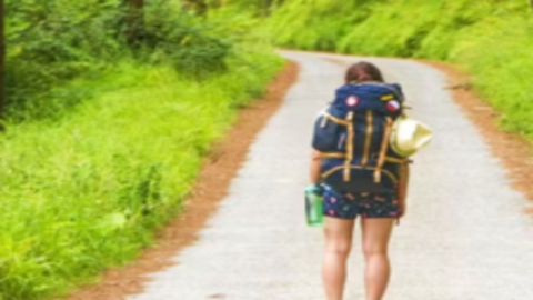Una viajera avanza con su mochila por un sendero desconocido, símbolo de quienes buscan un nuevo destino sin dejar de cargar con su historia.