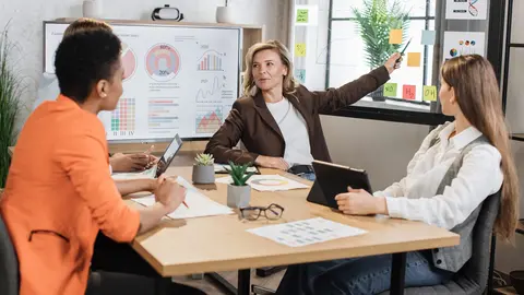 Tres emprendedoras comparten ideas y estrategias en una mesa de trabajo, ejemplo de las nuevas redes de apoyo que están creando las mujeres en Europa.