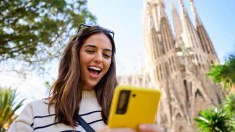 Una joven consulta su tel&eacute;fono m&oacute;vil frente a la Sagrada Familia de Barcelona, una de las ciudades espa&ntilde;olas que concentra un creciente n&uacute;mero de n&oacute;madas digitales en 2026.