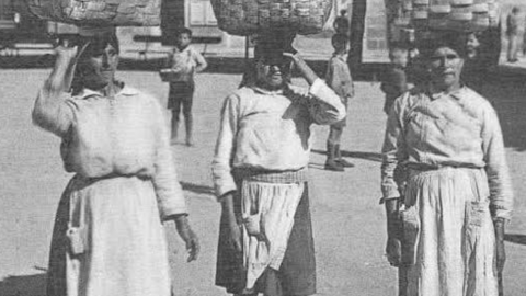 Tres mulleres transportan grandes cestos sobre a cabeza nunha imaxe hist&oacute;rica que testemu&ntilde;a a dureza do traballo feminino no rural galego, onde a forza, o equilibrio e o esforzo formaban parte da vida coti&aacute;.