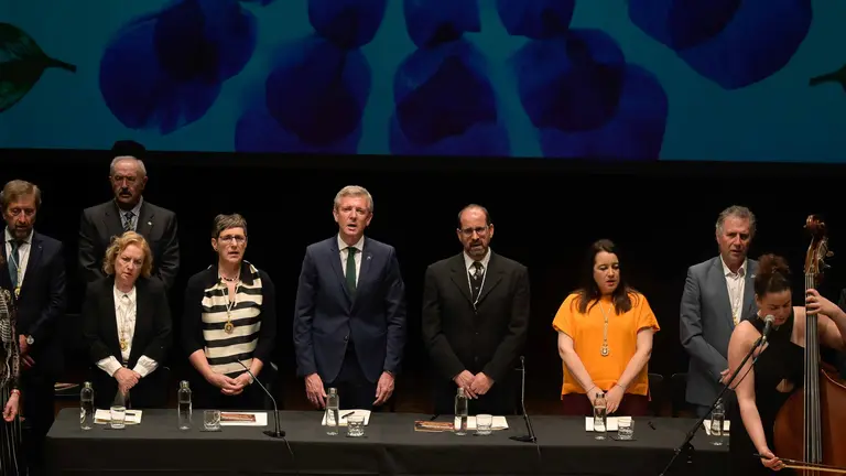 Representantes da Real Academia Galega e autoridades asistentes ao pleno extraordinario do D&iacute;a das Letras Galegas 2026, dedicado &aacute; escritora e xornalista Bego&ntilde;a Caama&ntilde;o, durante a celebraci&oacute;n no Teatro Principal de Santiago de Compostela.