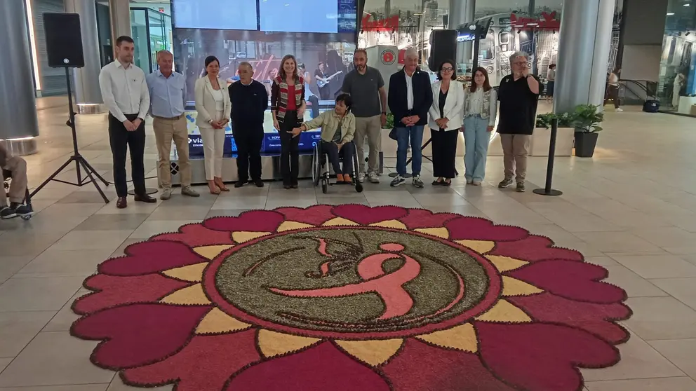 Representantes institucionales, entidades sociales y miembros de la Asociaci&oacute;n de Alfombristas do Corpus Christi de Ponteareas posan junto a la alfombra floral solidaria instalada en Vialia Vigo, dedicada a la lucha contra el c&aacute;ncer de mama.