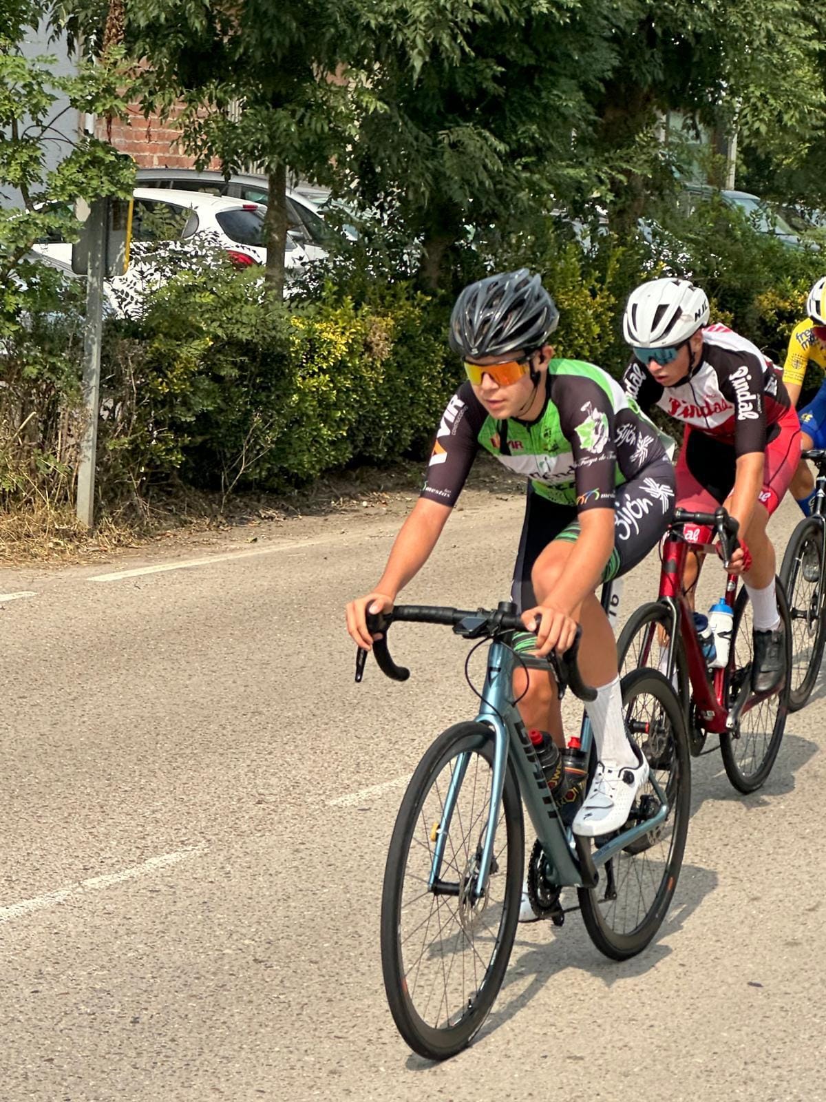 El corredor juvenil de Las Mestas pedaleando en una prueba de carretera, bajo la supervisión de su equipo.