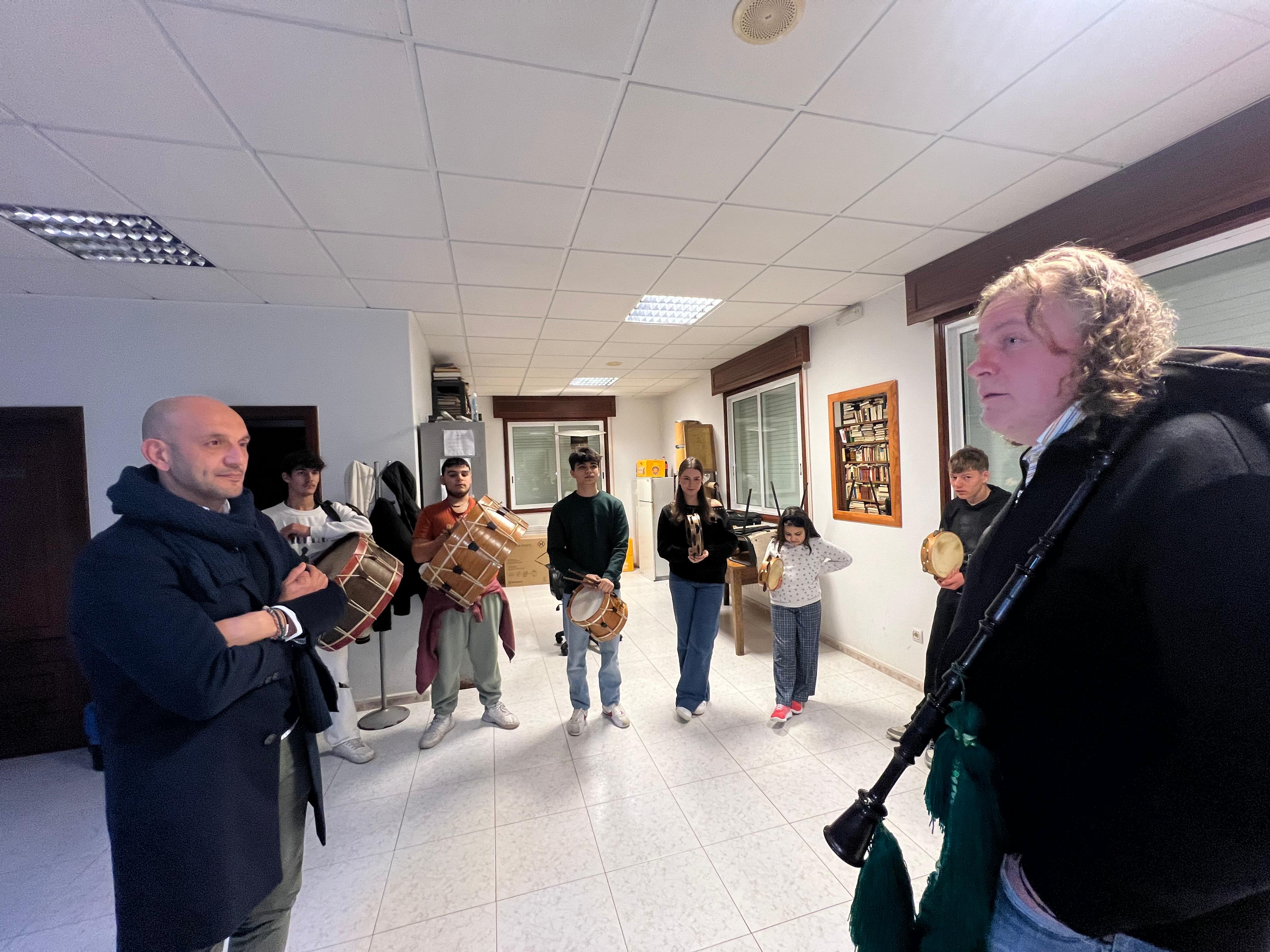 Ensaio dun grupo interxeracional de músicos tradicionais, con participación de nenos e mozos, durante unha sesión formativa dedicada á aprendizaxe do ritmo e dos instrumentos de percusión galegos.