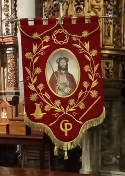 Estandarte de la Hermandad del Cristo Resucitado para la procesión de la Santa Cena, con fondo rojo y simbología de la Pasión como la corona de espinas y la caña del Ecce Homo.