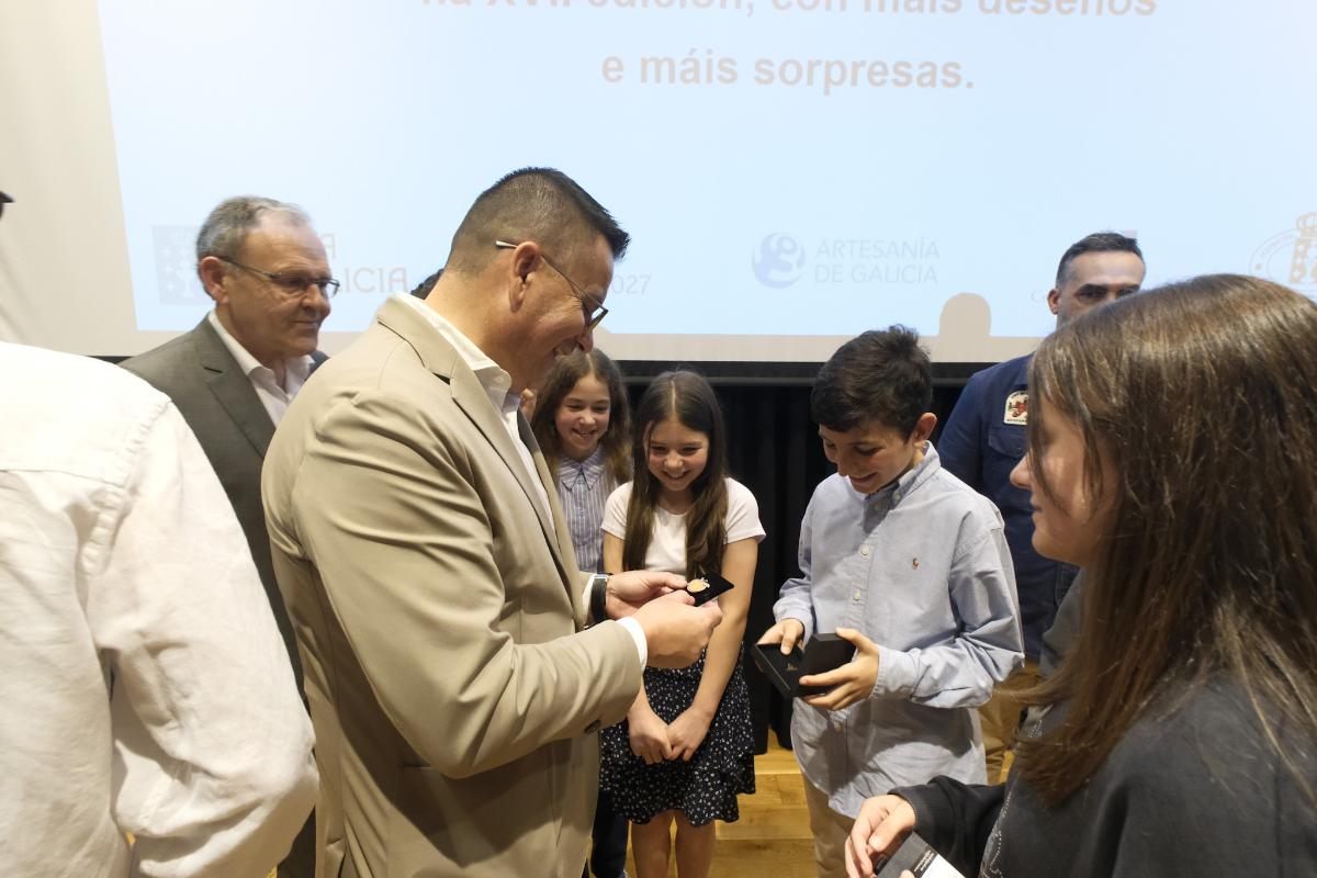 El conselleiro José González entrega uno de los premios del certamen infantil de joyería en Santiago, acompañado por varios participantes.