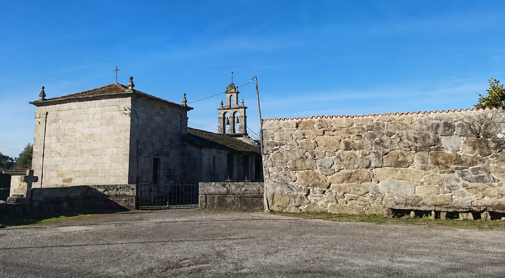 Vista exterior da igrexa parroquial de Santa Mariña desde a praza, coa cabeceira do templo, a espadana e o muro do recinto.