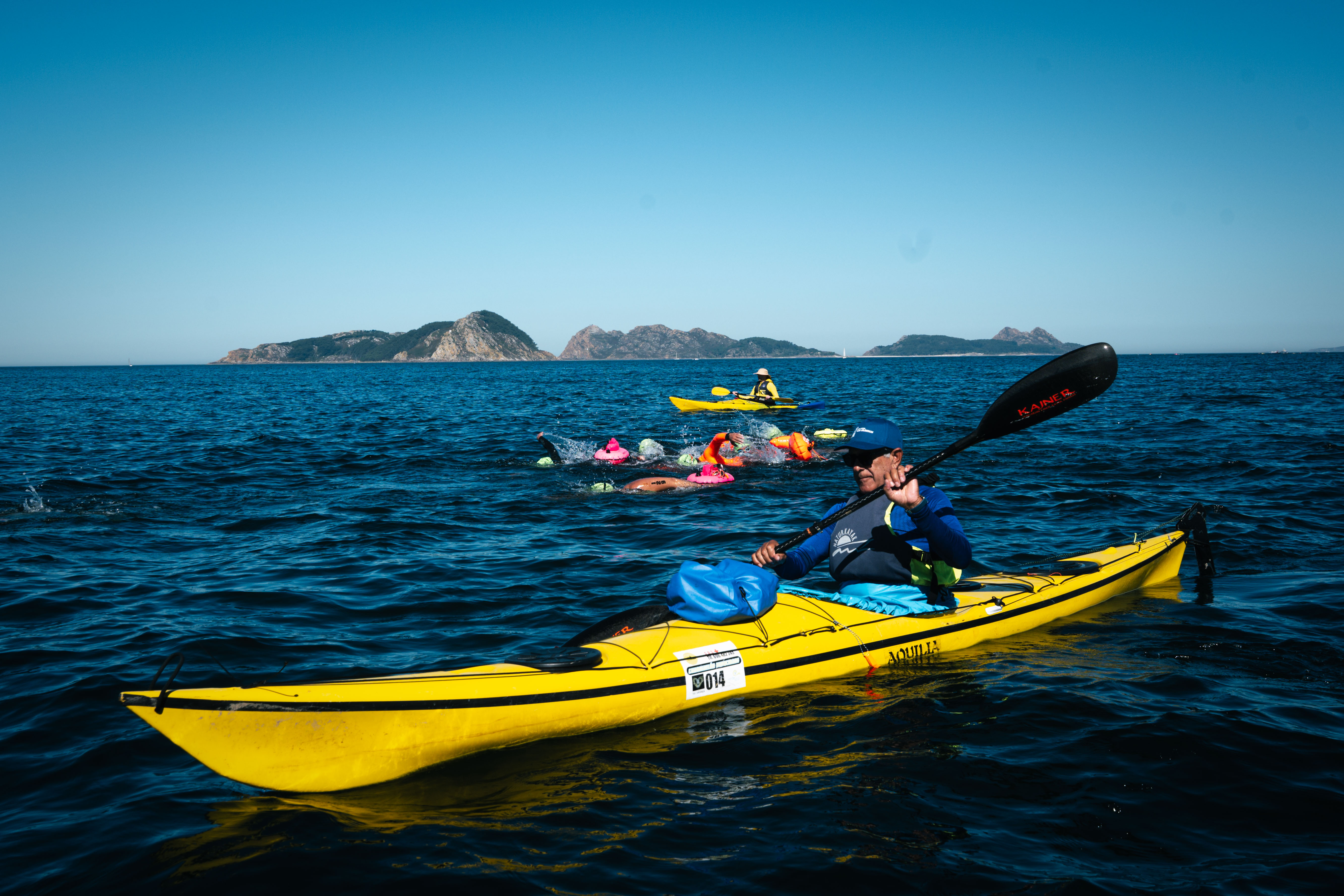 La travesía Cíes-Baiona, bajo vigilancia desde el mar: uno de los kayakistas del dispositivo de seguridad acompaña a los nadadores durante los 15 kilómetros de recorrido, con las islas Cíes al fondo.